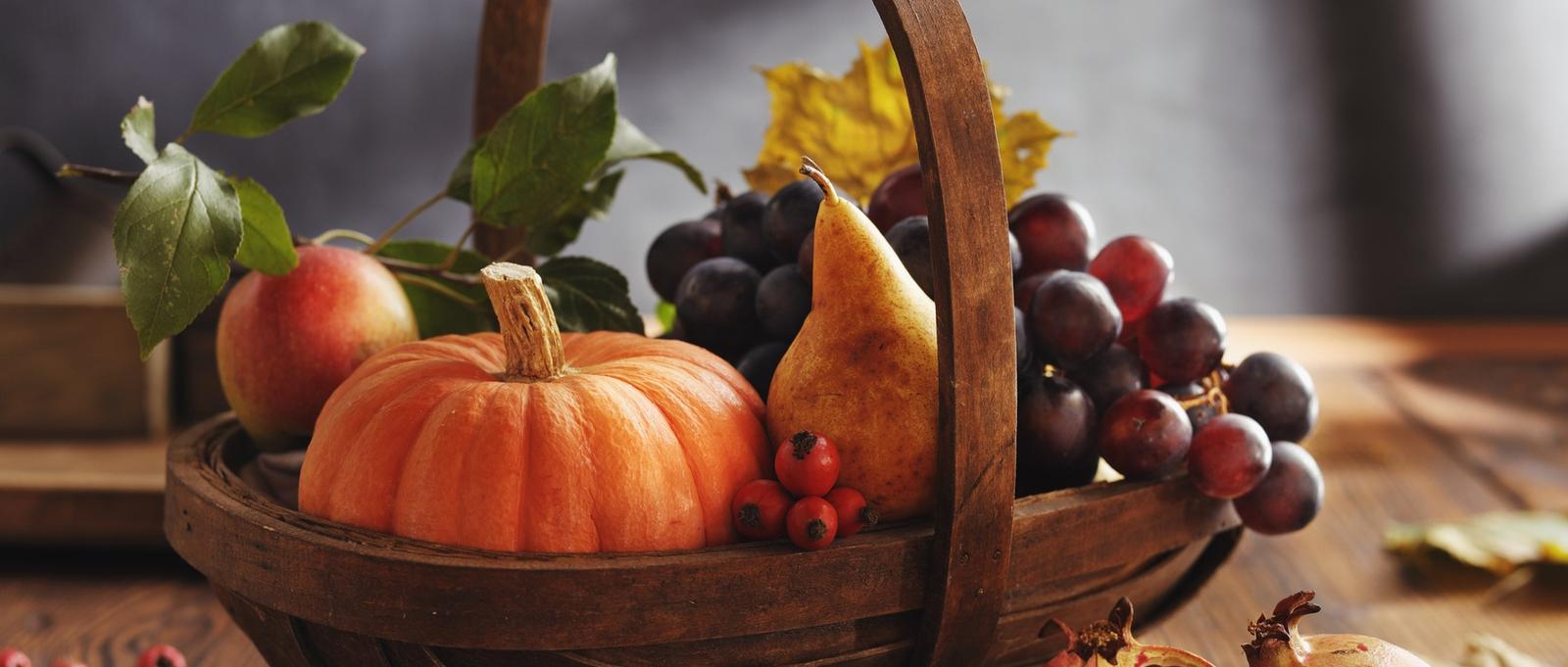 Holzkorb gefüllt mit Herbsternte wie Kürbis, Birne, Apfel, Trauben und Beeren mit Herbstlaub.