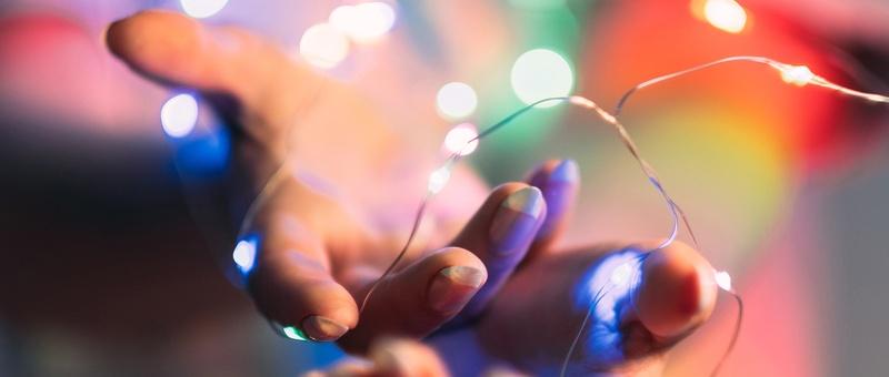 Coloured fairy lights wrapped around female hand against shadowy background.