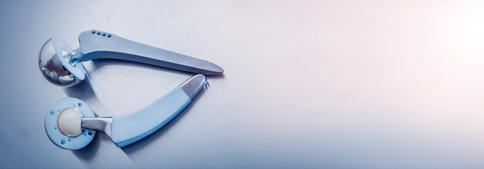 Medizinisches Gerät mit zwei metallischen Komponenten eines Gelenkimplantats auf hellblauem Hintergrund.