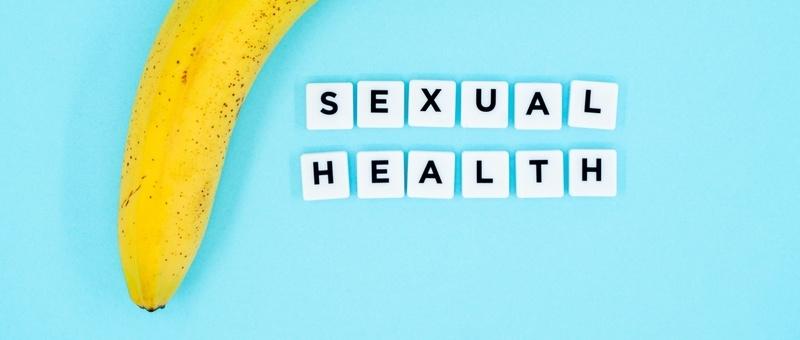 Typ geführt - SEXUELLE GESUNDHEIT auf weißen Blöcken neben einer Banane auf blauem Hintergrund gedruckt.