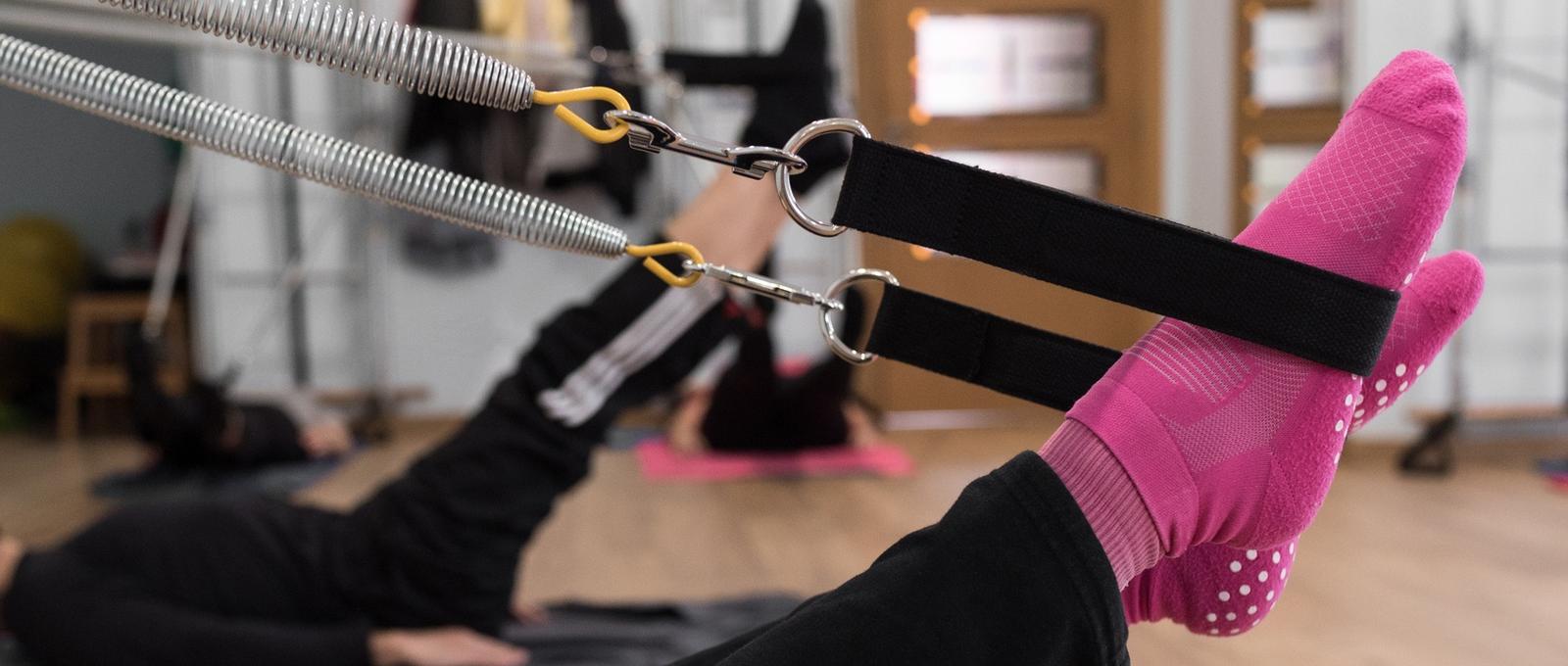 Anonyme Frau in hellen Socken hebt die Beine und dehnt die Federn während eines Pilates-Gruppentrainings im Studio