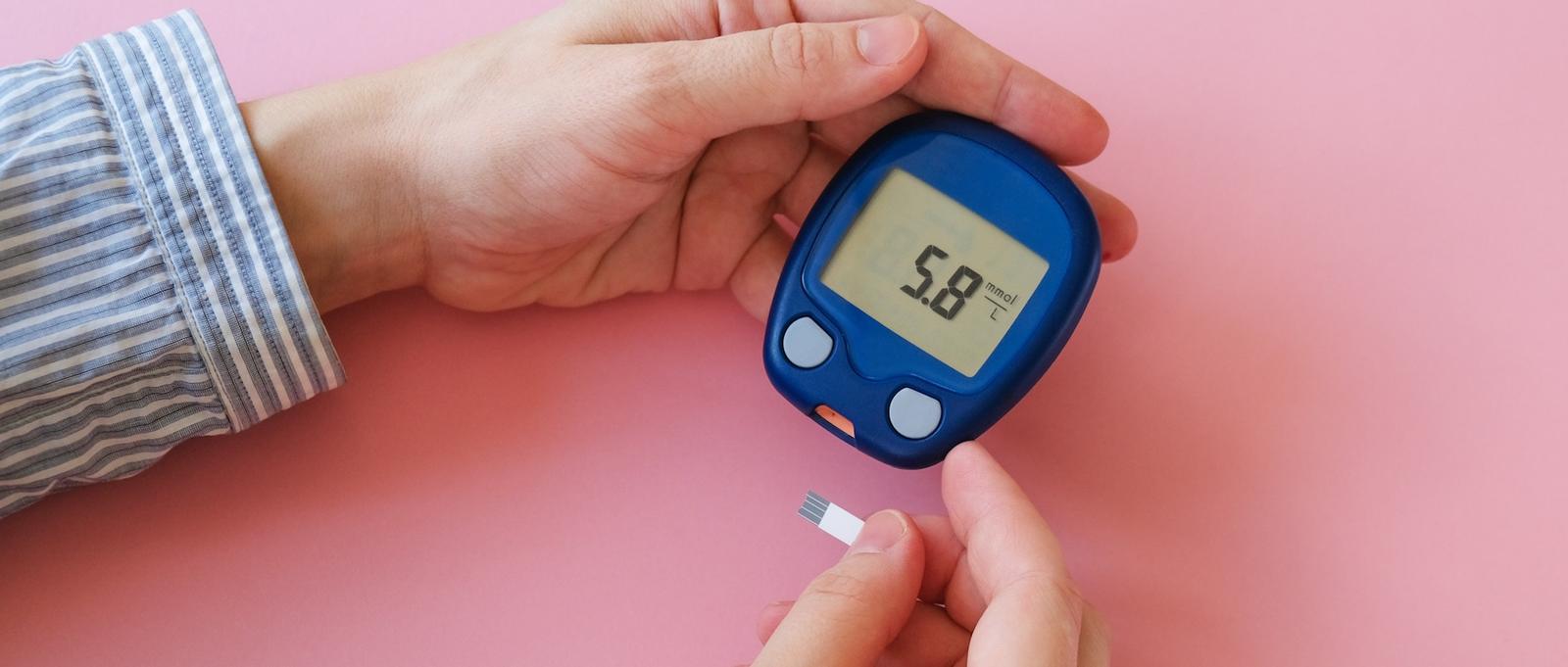 Nahaufnahme eines Paares von Händen, die ein Glukometer halten.