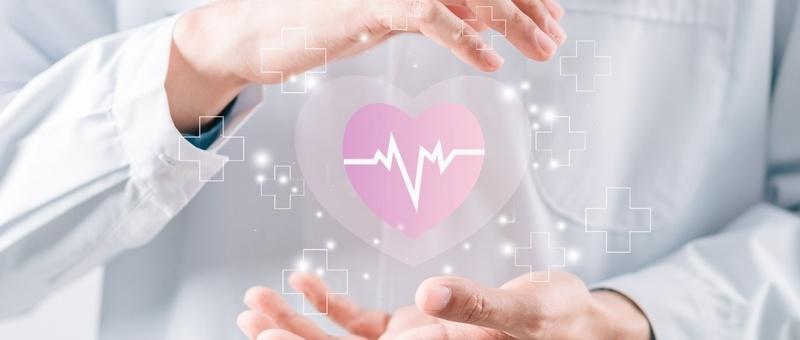 Die Hände einer medizinischen Fachkraft umgeben ein digitales rosa Herz mit Herzschlaglinie, umgeben von medizinischen Kreuzsymbolen.