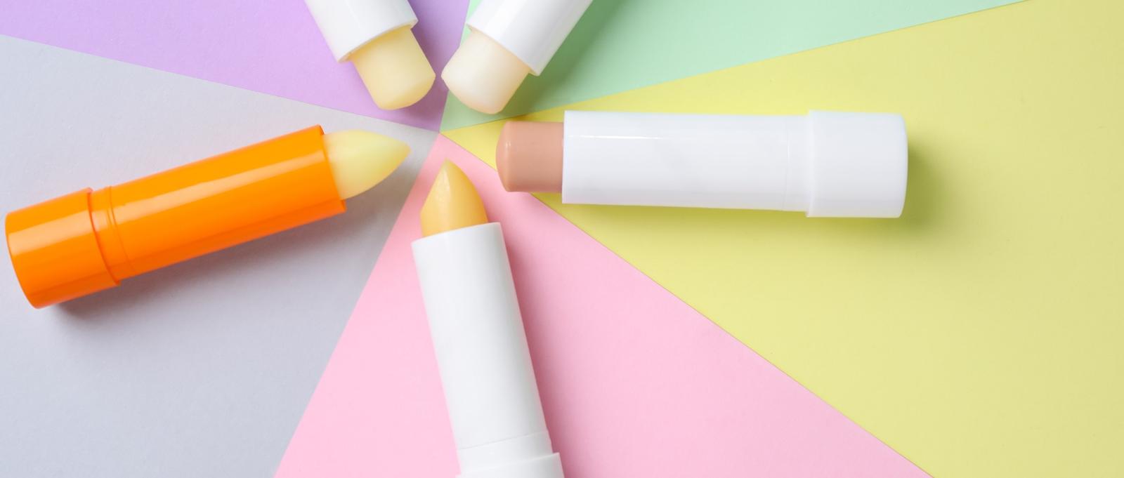 Bunte Lippenbalsame in einem Kreis auf pastellfarbenen Hintergrundabschnitten in Lila, Rosa, Gelb und Grün.