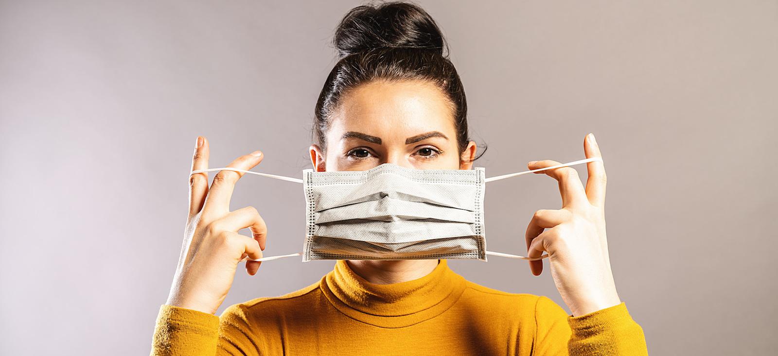 Eine Frau hält eine Maske über ihr Gesicht.