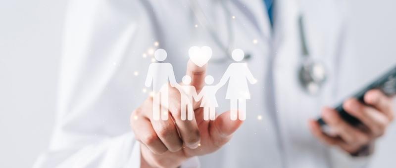 Medizinische Fachkraft in weißem Kittel, die ein digitales Familiensymbol hält, während sie in der anderen Hand ein Smartphone benutzt.