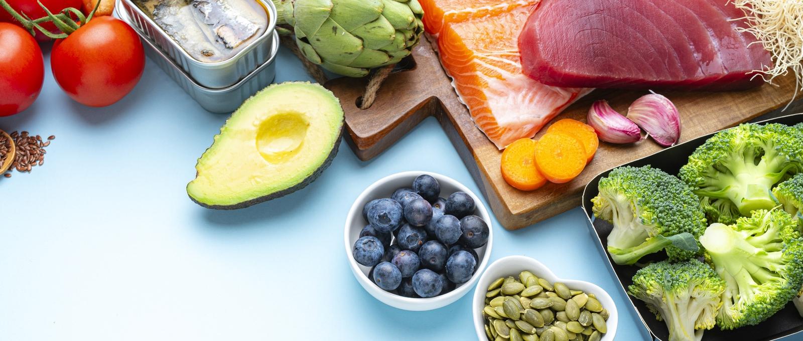 Lebensmittel, die bei langfristigen Entzündungen helfen, wie Fisch, Gemüse, Nüsse, Samen und Obst - alles vor blauem Hintergrund.