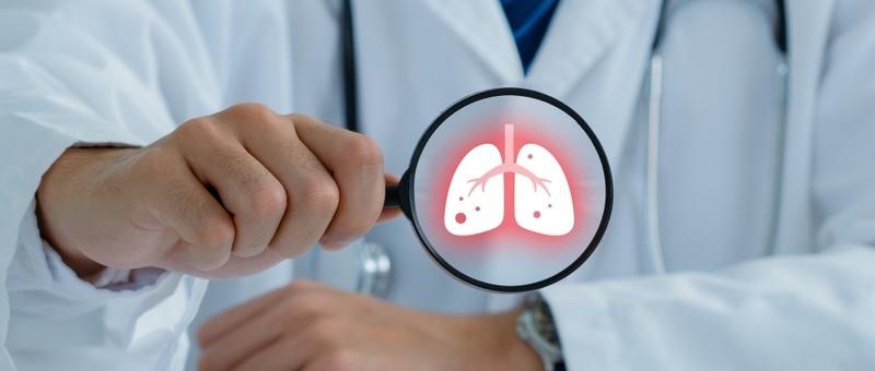 Medizinisches Fachpersonal in weißem Kittel hält ein Vergrößerungsglas, das eine leuchtende rote Lungenillustration zeigt