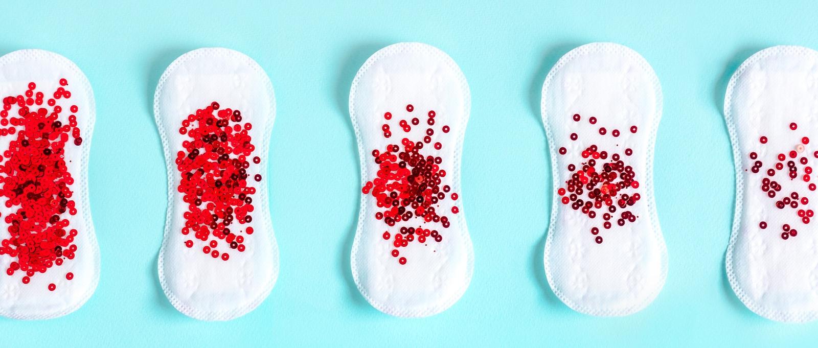 Menstruationsbinden mit rotem Glitzer auf blauem Hintergrund.