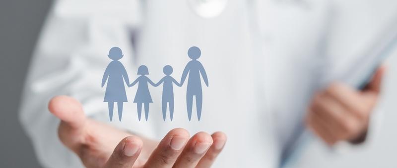 Die Hand hält eine blaue Silhouette einer Familie mit zwei Erwachsenen und zwei Kindern, die den Schutz der Familie symbolisiert.