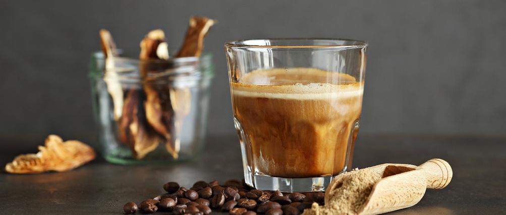Pilzkaffee in einem Glas, Kaffeebohnen und getrocknete Pilze auf dunklem Hintergrund.