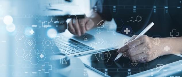 Eine Person arbeitet an einem Laptop und einem digitalen Tablet mit medizinischen Symbolen und Grafiken aus dem Gesundheitswesen, die in Blautönen überlagert werden.