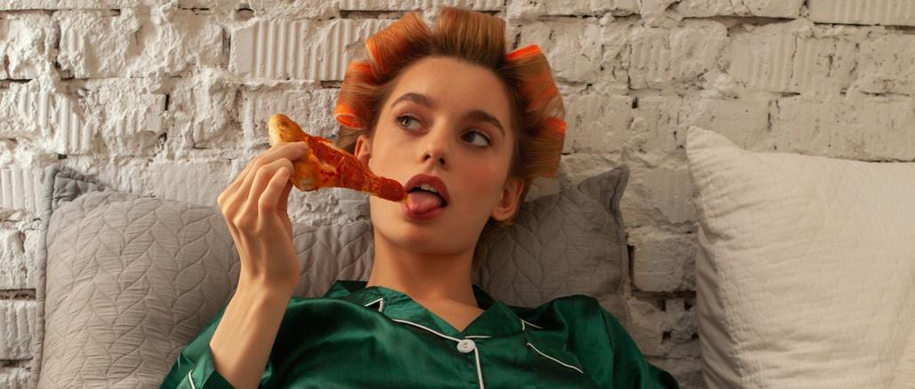 young fashionable woman in pyjamas with pizza box in bed at home