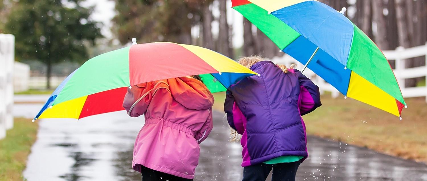 Kinder spielen in Pfützen und halten Regenschirm