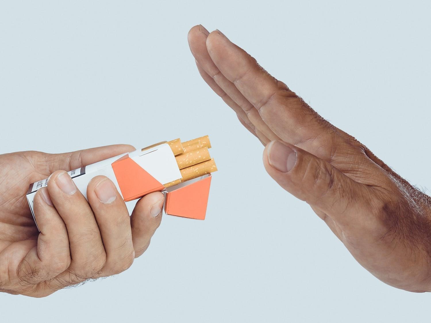 Die Hand gestikuliert "Stopp" zu einer anderen Hand, die eine Zigarettenschachtel anbietet, um den Rauchstopp oder die Ablehnung zu symbolisieren.