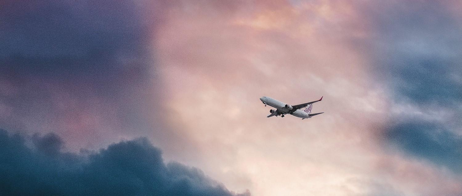 Ein Flugzeug von Virgin fliegt durch einen dramatischen rosa und blauen Wolkenhimmel in der Abenddämmerung.