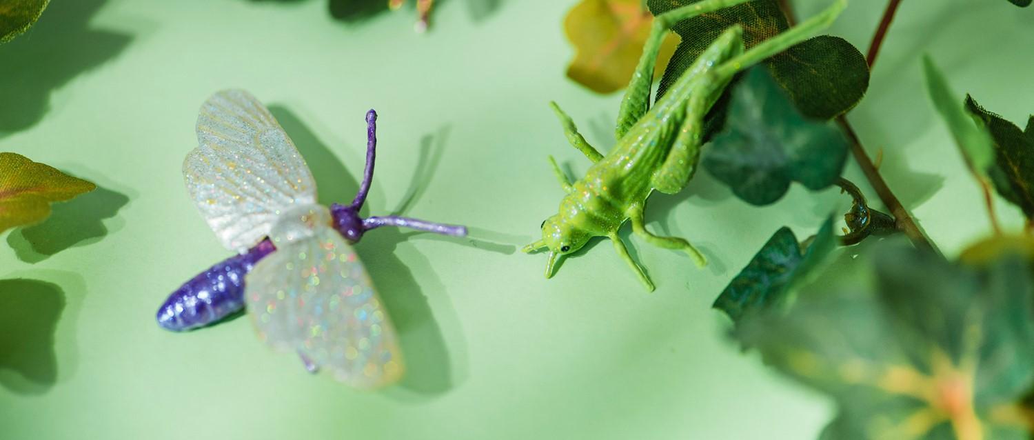 Dekorative Spielzeuginsekten auf grünem Untergrund - ein lila Schmetterling mit funkelnden Flügeln und eine leuchtend grüne Gottesanbeterin.