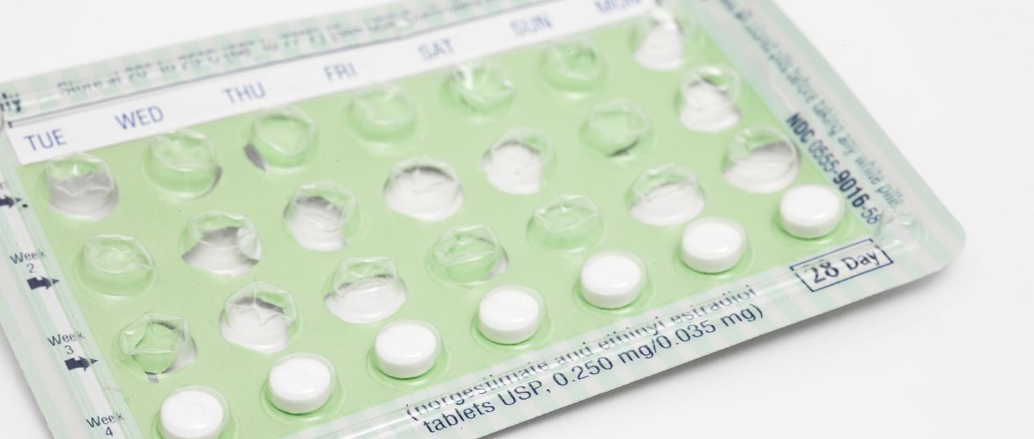 Birth control tablets pill pack with green backing showing days of the week and several white tablets in blister packaging.