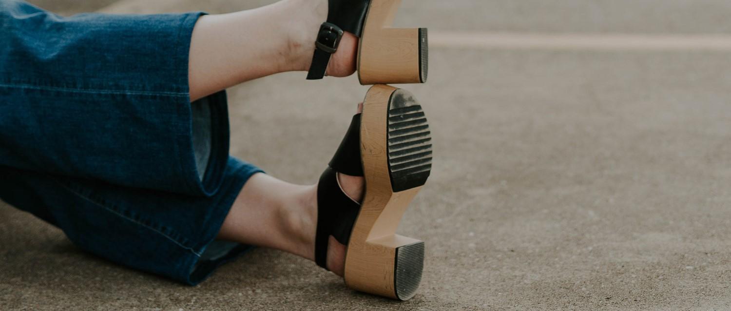 Person, die blaue Jeans und schwarze Sandalen mit Holzabsätzen mit Lipodema trägt, mit einer schwarzen Uhr am Handgelenk.