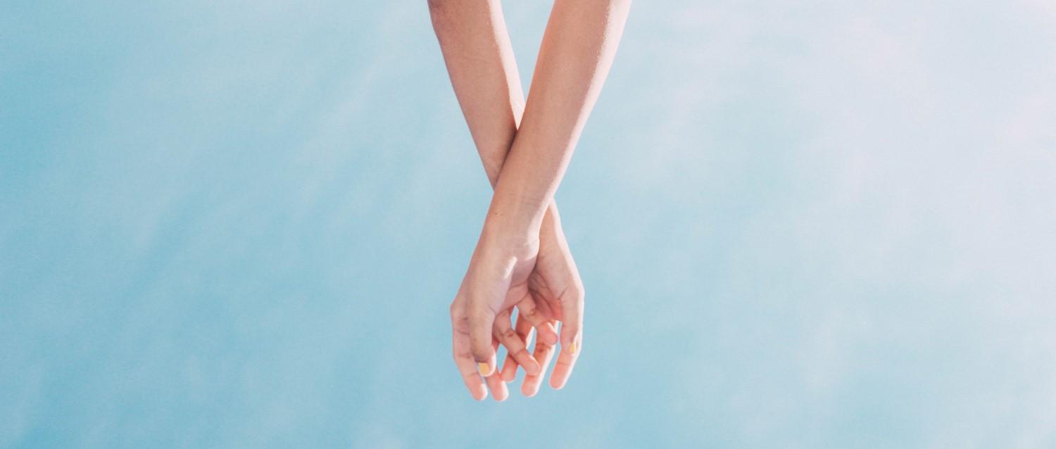 Zwei Hände berühren sich sanft mit ineinander verschlungenen Fingern vor einem hellblauen Hintergrund, der Intimität und Verbundenheit ausdrückt.