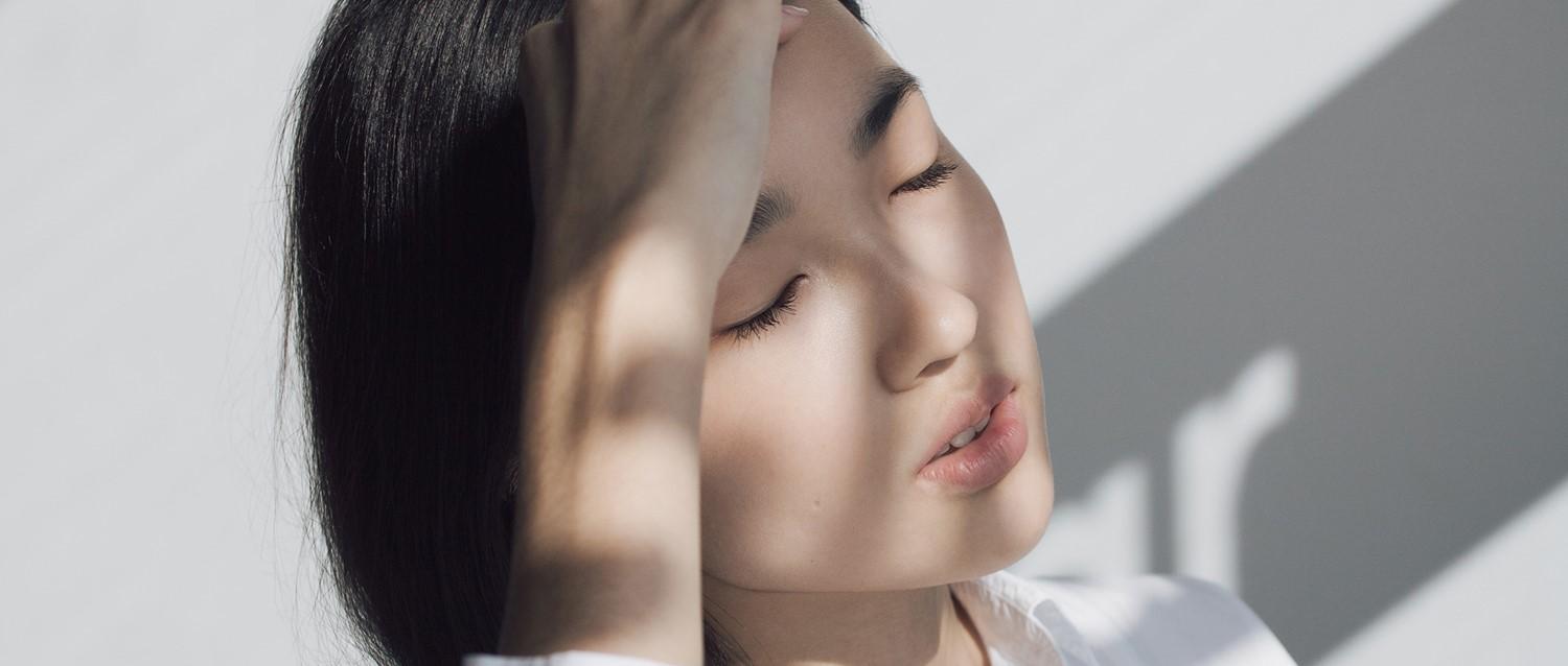 Person mit dunklem Haar und geschlossenen Augen in weichem Licht, wobei die Schatten eine ruhige, friedliche Atmosphäre schaffen.
