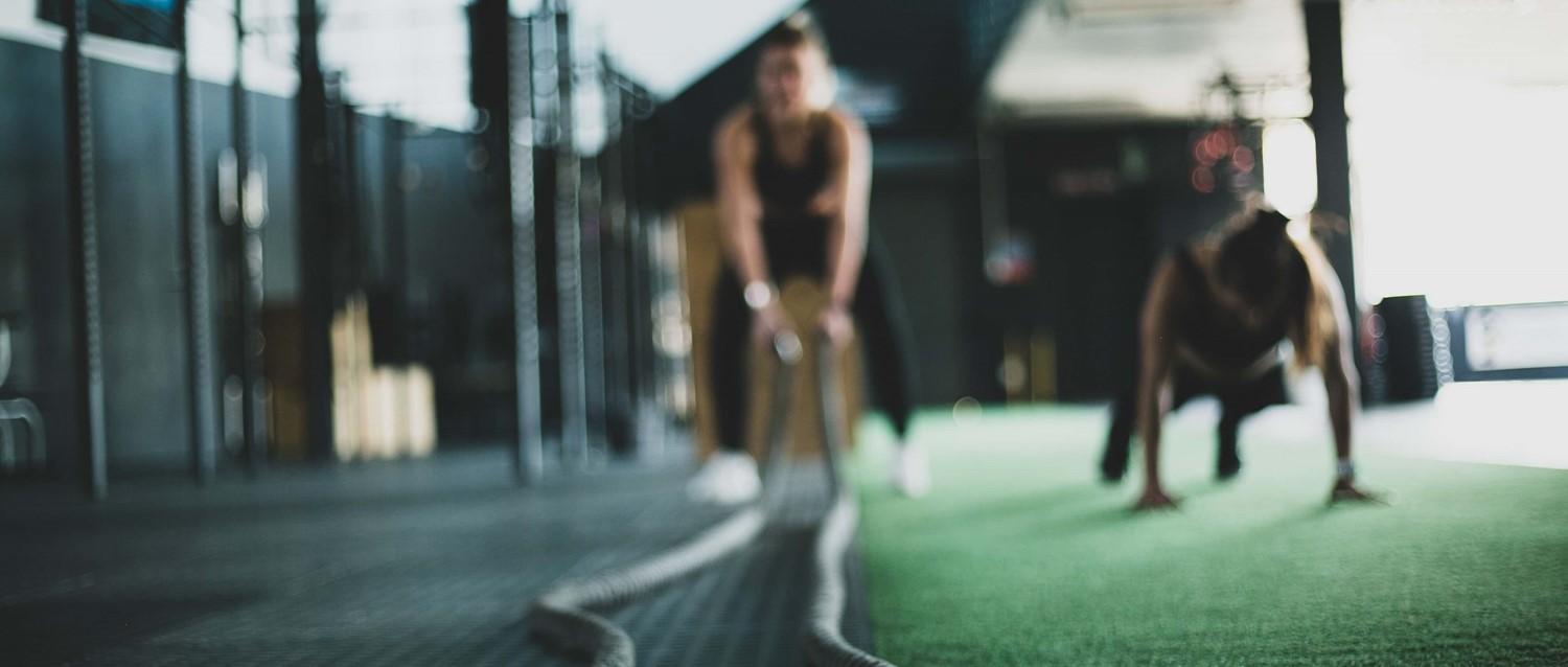 Unscharfe Figuren trainieren in einem modernen Fitnessstudio mit grünem Bodenbelag und konzentrieren sich auf Krafttraining in einer dunklen Umgebung.