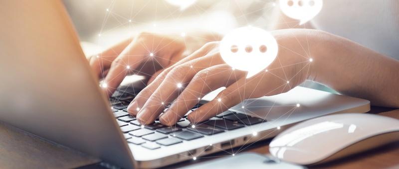 Hände, die auf einer Laptop-Tastatur tippen, mit eingeblendeten digitalen Sprechblasen und Netzanschlusspunkten, die auf Online-Kommunikation hindeuten.