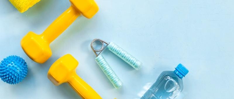 Yellow hand weights and various blue fitness equipment beside clear plastic water bottle against pale blue background.